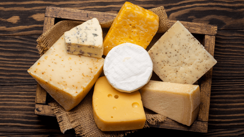 an assortment of cheese blocks & wedges on a rustic wooden board, including blue cheese, brie, yellow cheddar