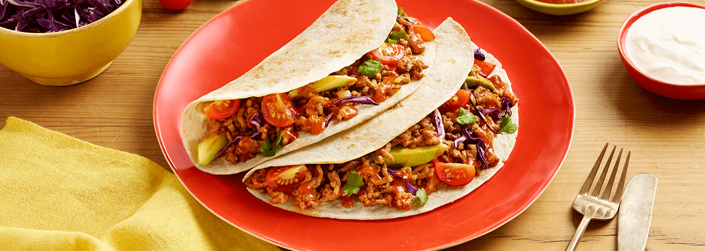 classic fiery beef tacos served on red plate accompanied by fork & knife