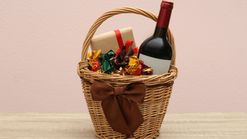 a basket having wrapped gifts & wine bottle on a wooden table
