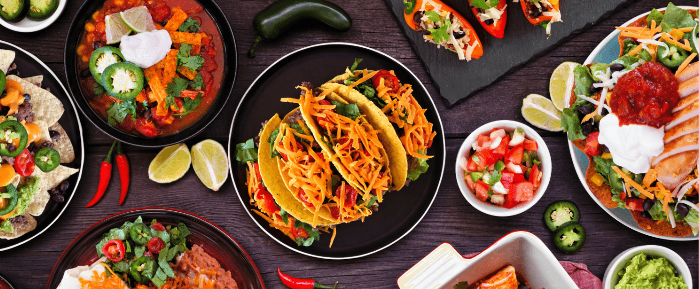 a spread of mexican dishes including tacos, fajitas, nachos, salsa & garnishes on a dark wooden table