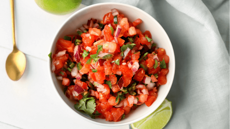 A chunkier raw salsa featuring tomatoes, onions, coriander, and lime juice served in a white bowl with a golden spoon