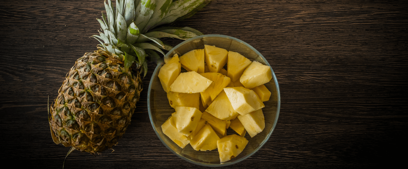 pineapple with chunks in a bowl on a dark wooden background