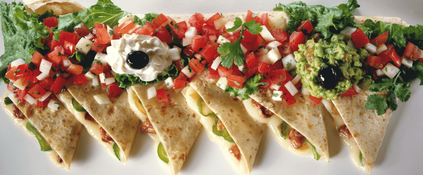 quesadillas topped with guacamole & sour cream garnished with tomatoes on rustic white background