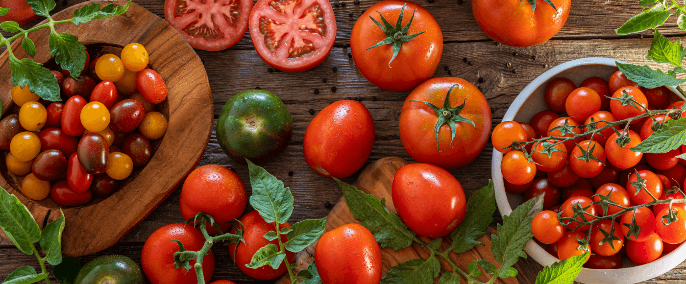 assorted tomatoes, including whole, sliced & cherry varieties, arranged on a rustic wooden table & a white bowl