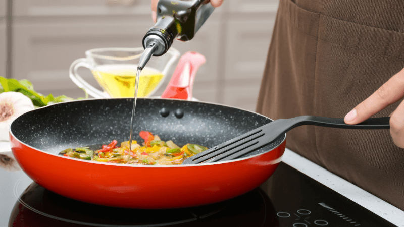 a hand pouring oil into red frying pan on a stovetop