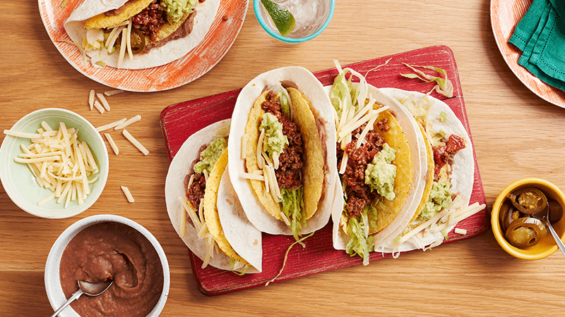 beef tacos served on red borad with cheese, salsa