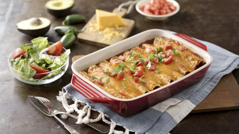 enchiladas in a tray placed on cloth on wooden table
