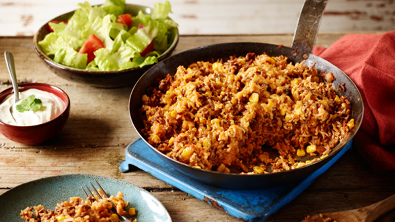 skillet with beef taco rice, served with salad & sour cream on a rustic wooden table