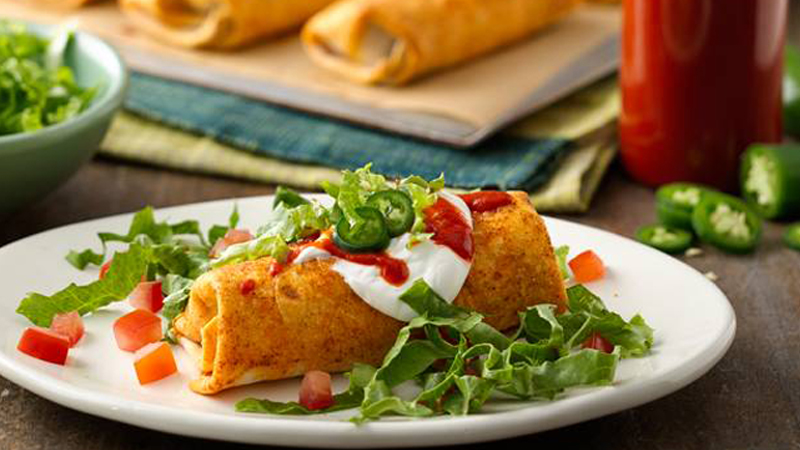 Sriracha Beef Burritos served in a white plate topped with sour cream, shredded lettuce & diced tomatoes