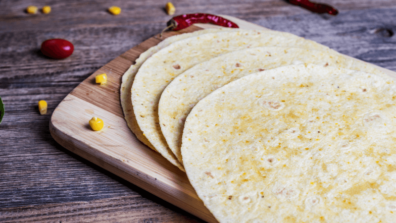 mexican tortillas placed on wooden board with dry chilies & corn kernels around