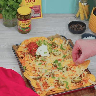 cheesy nachos served on a baking tray topped with salsa & sour cream